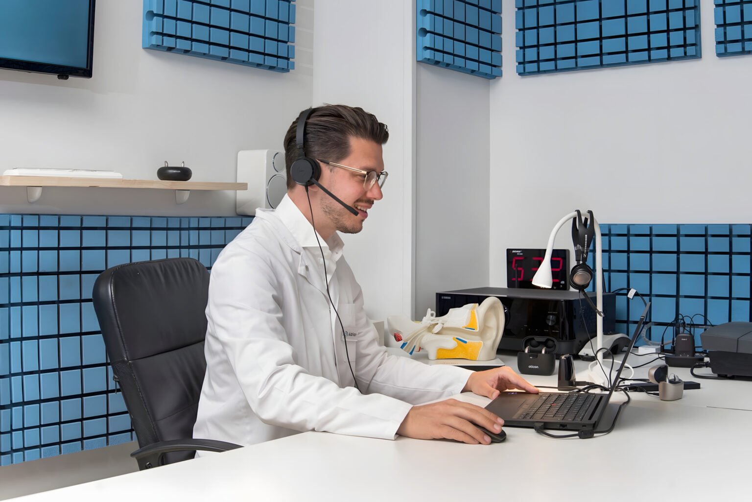 Hörakustiker von Best Price Hearing mit Audiometrie-Kopfhörer vor der schallisolierten Messkabine